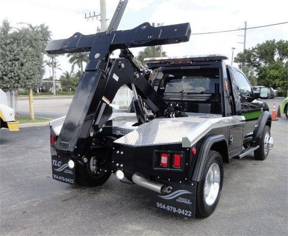 Ram 4500 HD tow truck rear view with hydraulic wrecker arm and flatbed, black with diamond plate bed and towing equipment.