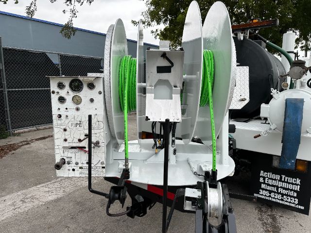 Truck body with two large spools of bright green hose mounted on a reel system and control panel labeled FIRE, attached to a vacuum truck setup.
