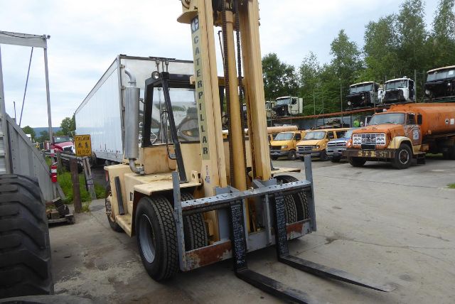 Caterpillar V225 forklift in a yard, front view with forks down, beige body, black tires, other trucks in background.