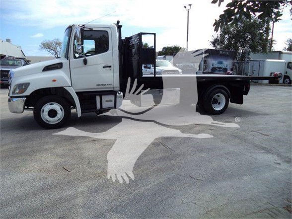 2017 Hino 258LP hooklift truck in a parking lot showing a white cab and flatbed with open cabin step area.