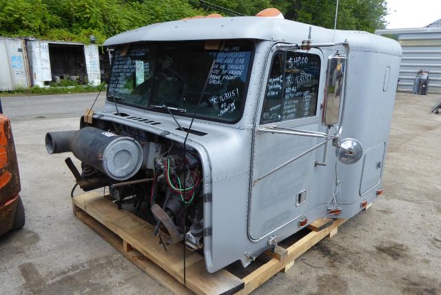 1991 Freightliner FLD120 cab with engine removed, gray exterior, on wooden pallet, showing exposed engine bay and wiring harnesses.