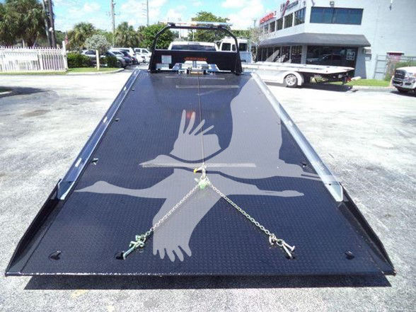 Ram 5500 tow truck with a large flatbed ramp, black diamond plate surface, center tie-down chain, and rear hitch points.