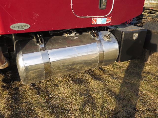 Peterbilt 388 fuel tank and underbody showing shiny cylindrical aluminum tank mounted under cab with fuel lines and a black toolbox nearby.