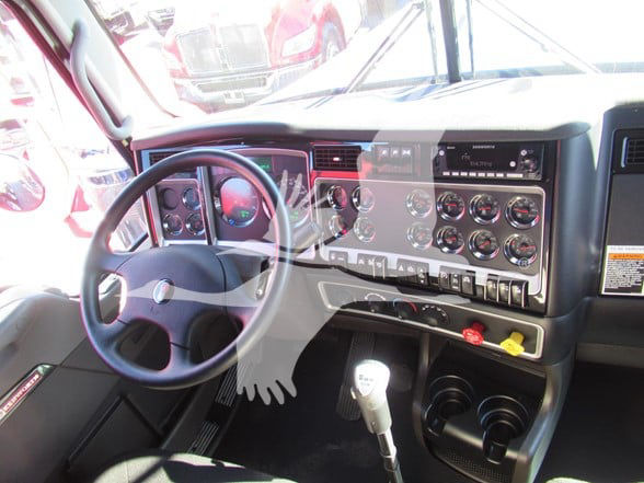 Truck cab interior showing steering wheel, dashboard with multiple gauges, gear shifter, and auxiliary controls.