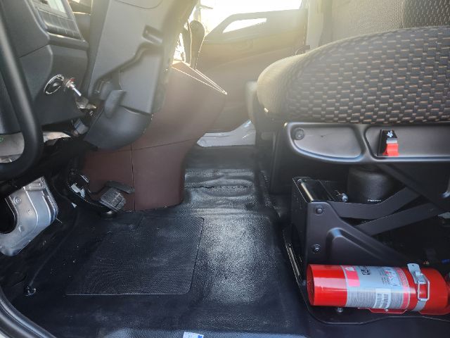 Interior cab view of a 2025 Hino L6 box truck showing front passenger seat, floor mats, pedal area, and a red fire extinguisher on the right.