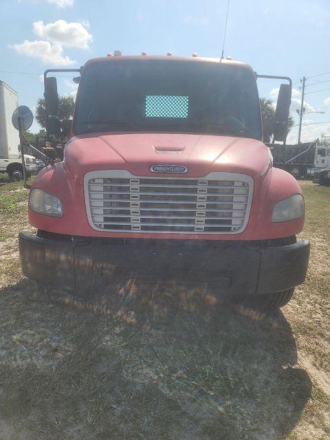 Freightliner M2 front view showing pink cab, large chrome grille, bumper, and headlights. Windshield with a dotted sunshade in center. No visible text other than truck branding.
