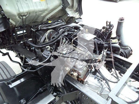 Isuzu NPR HD engine bay showing exposed diesel engine with belts, hoses, and intake components.