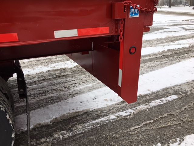 Red trailer with a chain and sticker visible at the hitch area; snow on ground; vertical red post with circular reflectors.