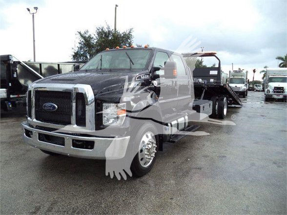 Ford F-750 SD tow truck daytime view showing front grille, cab, and flatbed behind.