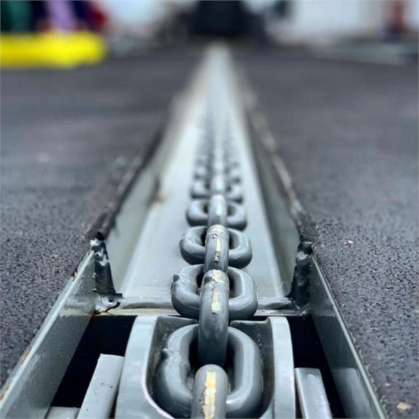 View of a drop deck container trailer chain tie-down track with heavy steel hooks along the centerline.