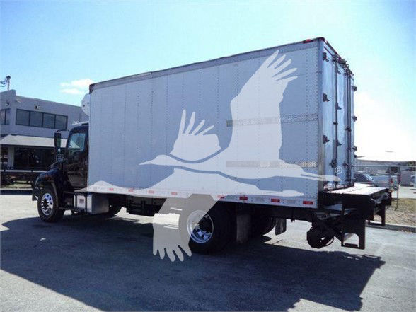 Truck with a refrigerated box, side view, white cargo trailer attached to a black cab; stock yard setting.