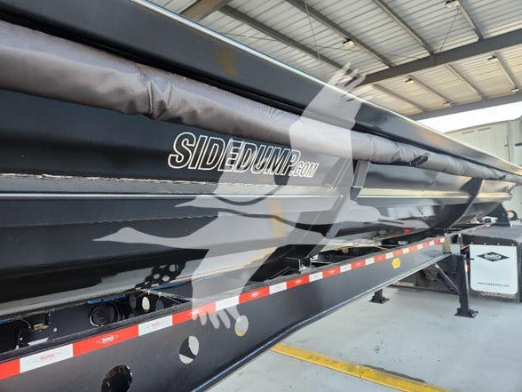 Side view of a new Smithco dump trailer with 'SIDEDUMP.com' logo visible on the side and reflective red-and-white safety strip along the lower edge.