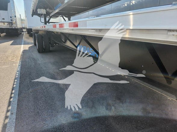 Flatbed trailer side view showing Wabash branding and vehicle undercarriage details.