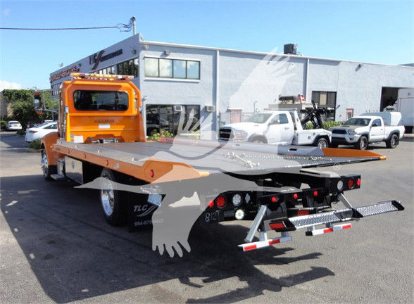 Truck bed of a 2022 Peterbilt 337 tow truck with a bright orange cab and flatbed in a dealership lot.