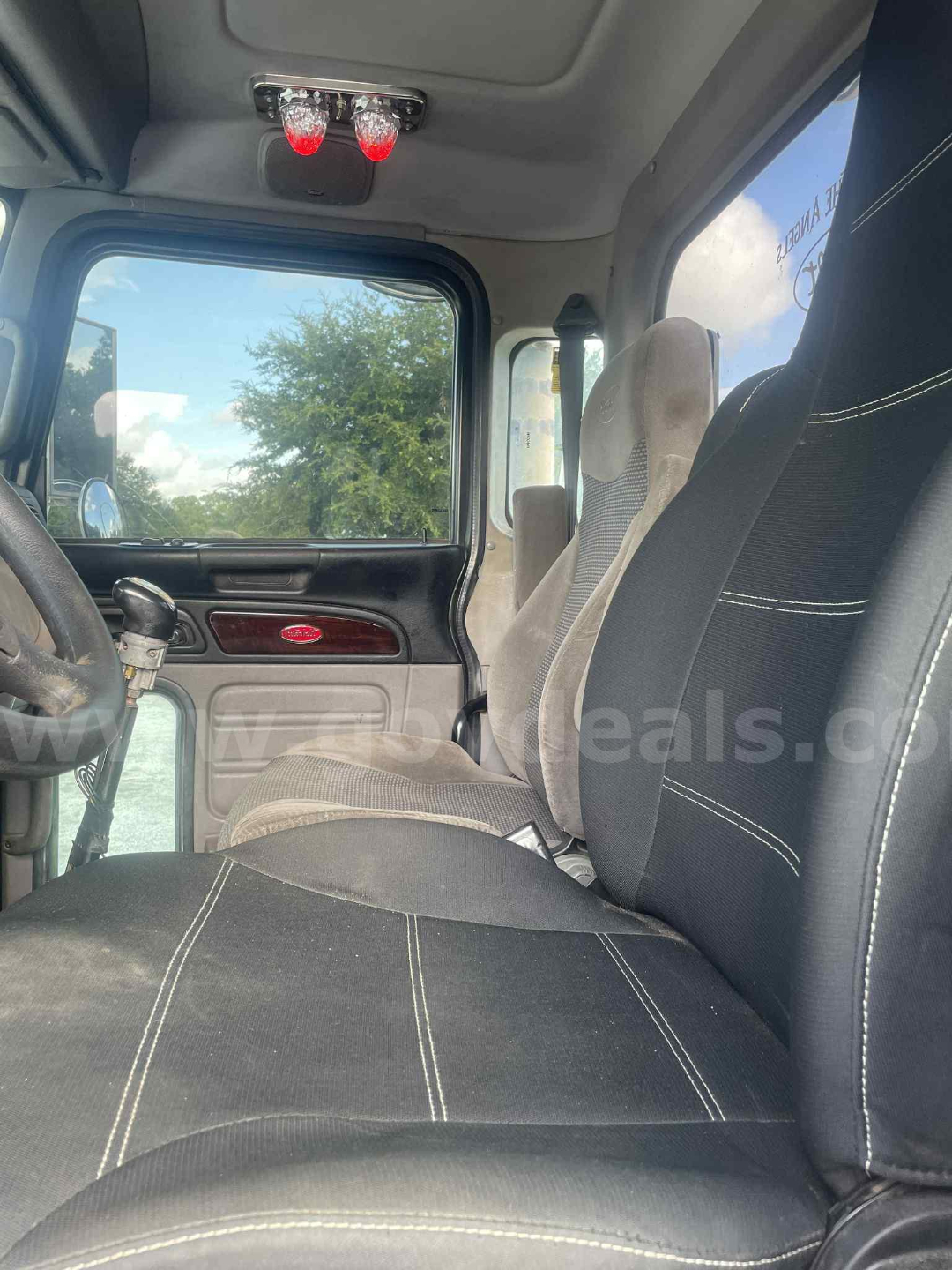 Peterbilt 386 cab interior showing front seats, steering column, dashboard with wood trim, and overhead dome lights.