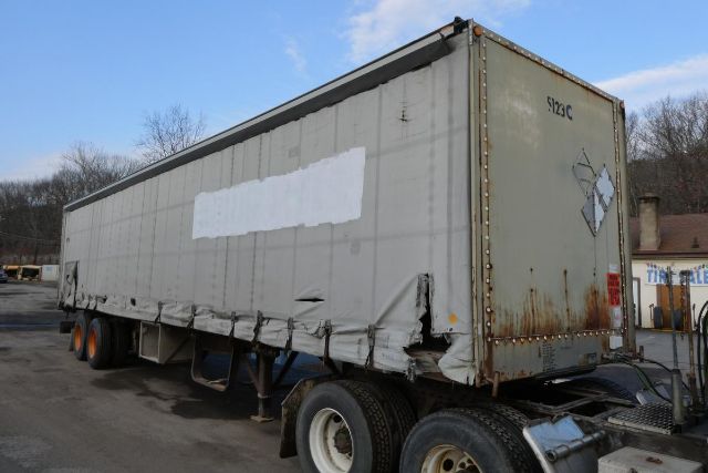 Curtainside trailer showing worn exterior with rust on rear door and undercarriage, side panels, and dual rear wheels.
