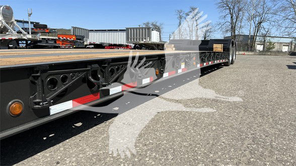 Lowboy trailer showing side rail, hydraulic lines, and reflective tape along length; caption text not visible in image.
