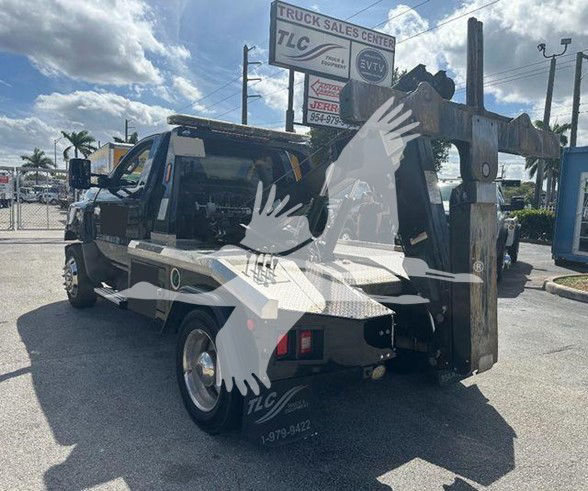 Tow truck with boom and crane attachment in rear, text on sign 'TRUCK SALES CENTER' visible in background.