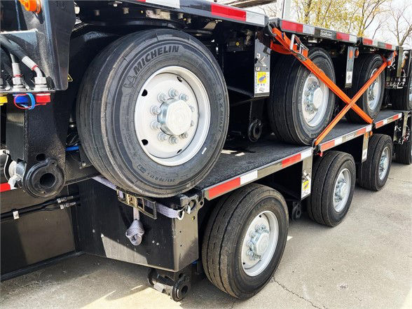 Trailer axle and wheels on a multi-axle deck trailer showing Michelin tire and silver steel wheel rims.