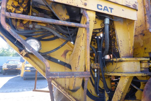 Caterpillar 16G grader front frame and hydraulic lines with CAT branding visible; yellow paint, wiring harnesses, and rugged metal framework.