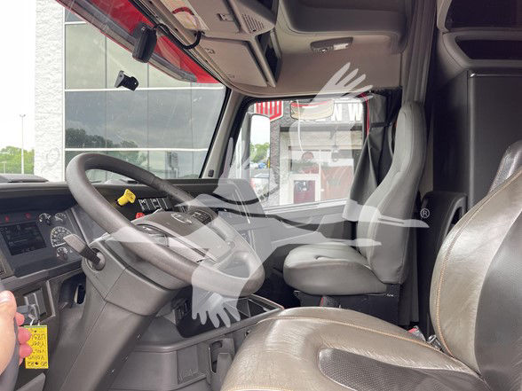 Interior of a Volvo VNL64T740 truck cab showing steering wheel, driver's seat, and dashboard with pedals.