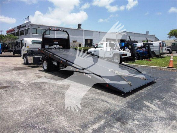 Isuzu NRR truck with a heavy equipment flatbed tow truck bed in a dealership lot.