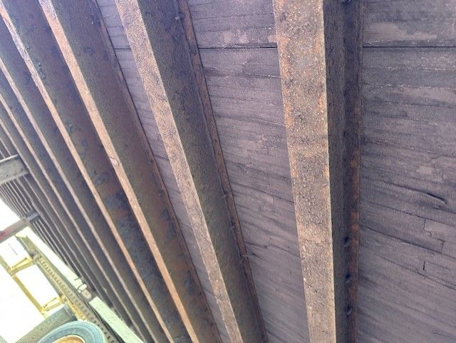 Trailer underside with dark metal joists and brown flatbed planks visible.