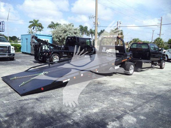 Tow truck with a flatbed trailer in a parking lot; International CV truck in background, branding not legible.