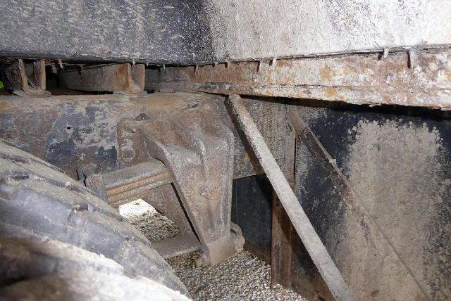 Underbody view of a bus chassis showing rusty metal frame and suspension components.