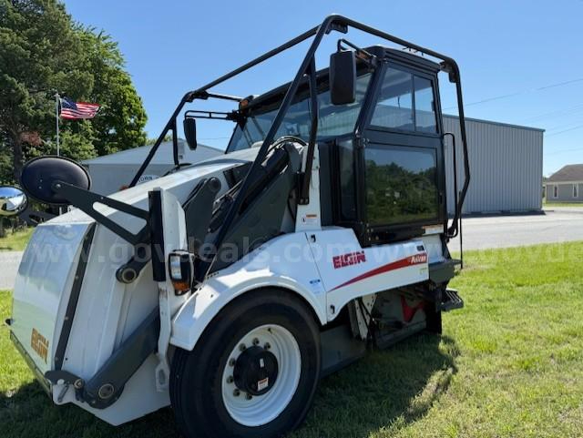 Elgin Pelican NP sweeper truck side view showing cab and front loader, white body with Elgin branding, black frame