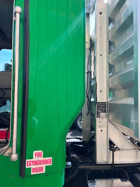 Truck cab with bright green front fender and door; a black vertical door seal; a label near the lower door edge; a white and red Fire Extinguisher Inside sticker on the green panel; a metal ladder and corrugated side with silver brackets.