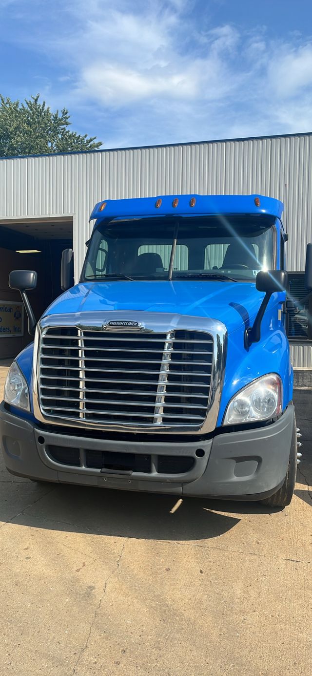 Freightliner Cascadia front view showing blue cab and chrome grille; large windshield, side mirrors, and grey bumper.