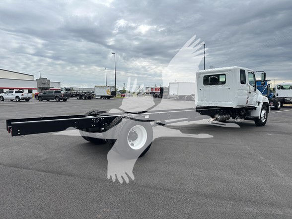 Truck cab and chassis with long flatbed-style frame, white cab, black chassis, in a dealership lot; faint watermark over image.