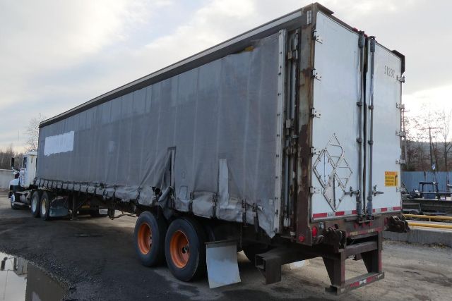 Curtainside trailer in a yard showing rear doors and triple-axle wheels with orange rims.