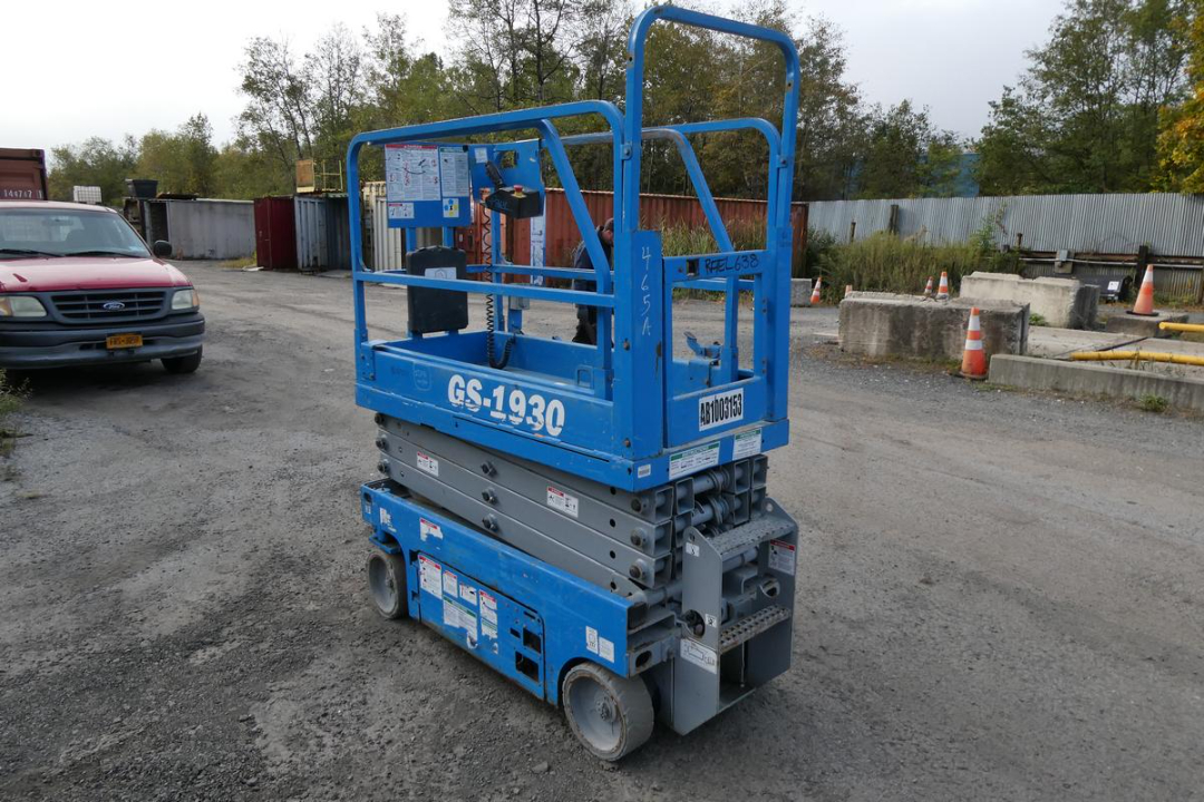 GS-1930 scissor lift in blue with guard rails, platform controls, and wheels; label GS-1930 on side and serial/identification plate visible.