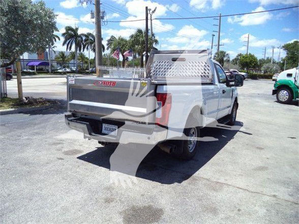 Truck bed with aluminum diamond plate toolbox and rear decal, white Ford F-250 dump truck in a parking lot.