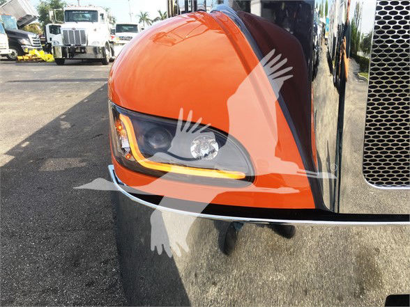 Peterbilt 337 truck front corner with orange hood and headlight, chrome grille on right, water reflection on bumper.