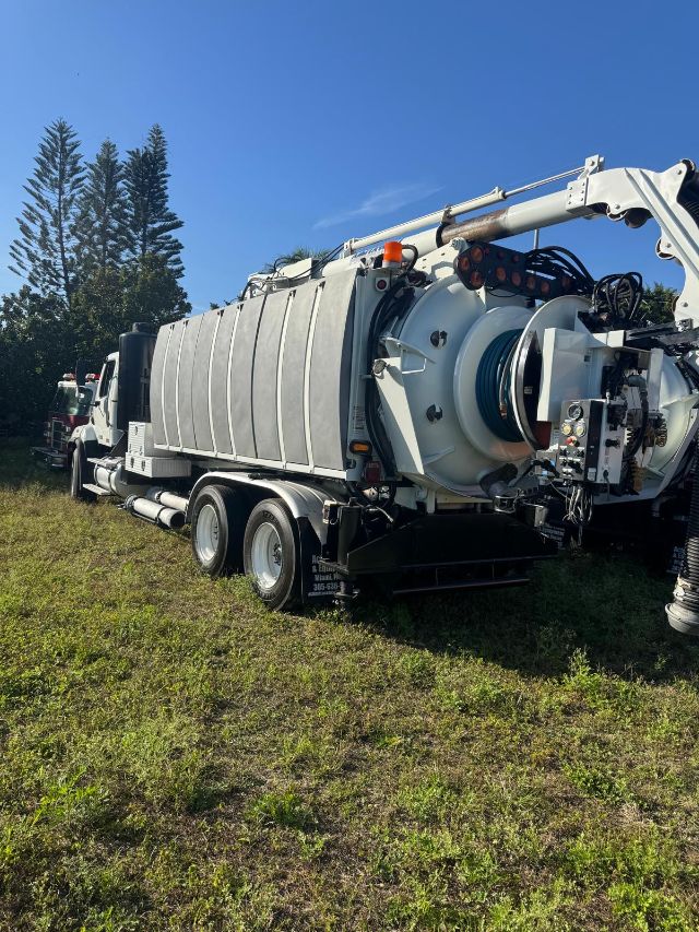 Truck-mounted vacuum tanker with large reel and hoses, Freightliner 114SD chassis in a grassy lot.