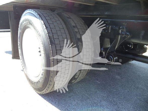 Truck rear wheel and suspension undercarriage with partial view of frame and components.