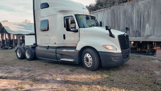 2019 International conventional sleeper truck in a yard, white cab with black bumper, two-axle trailer behind, visible wheel wells and side mirrors.