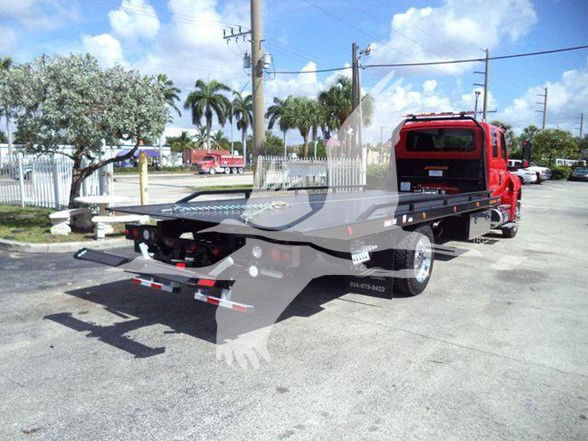 Tow truck with flatbed, rear view showing black flatbed, red cab, and towing equipment. No legible text visible.