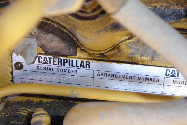 Caterpillar serial and arrangement number plate visible on yellow machinery with dirt and hoses around.
