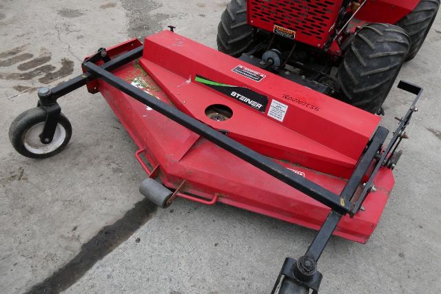 Steiner cutter/brush mower attachment in red with black bars and wheels, mounted behind a red vehicle. Visible text includes 'STEINER' on the side and model details on a white label.