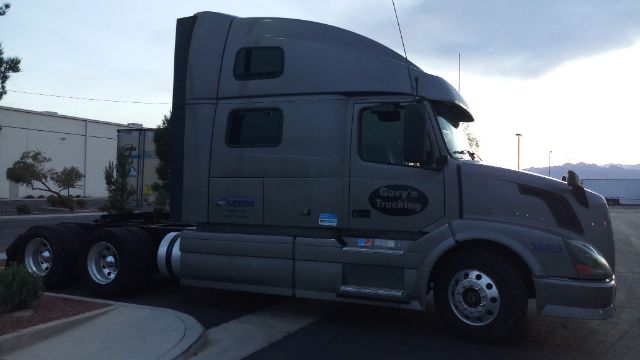 Volvo 780 conventional sleeper truck side view showing gray cab, sleeper compartment, and dual rear axles with chrome fuel tanks.