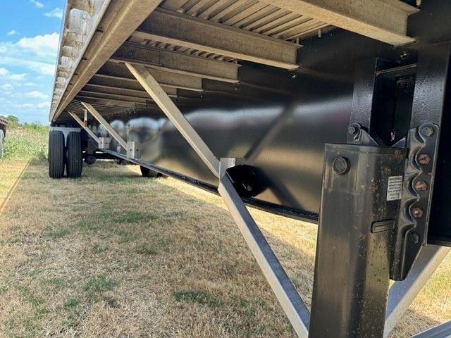 Flatbed trailer undercarriage showing black frame, support legs, and wheel tar, with light glare on metal surfaces.