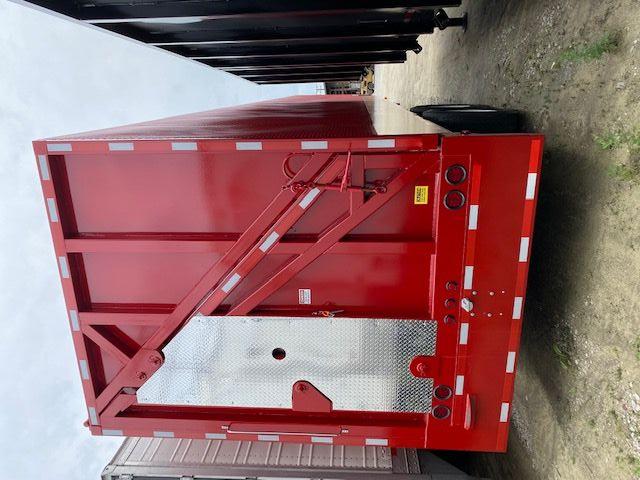 Crush car carrier trailer back view showing red two-axle trailer with diagonal brace, reflective white strips, and diamond plate access door.