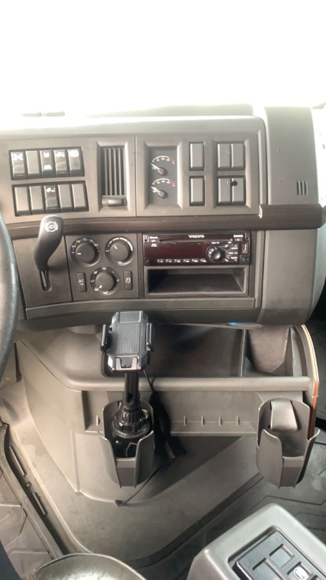 Dashboard of a 2019 Volvo VNL64T860 with controls, gauges, and a mounted device in the center console; includes climate controls, stereo, and a cup holder area.