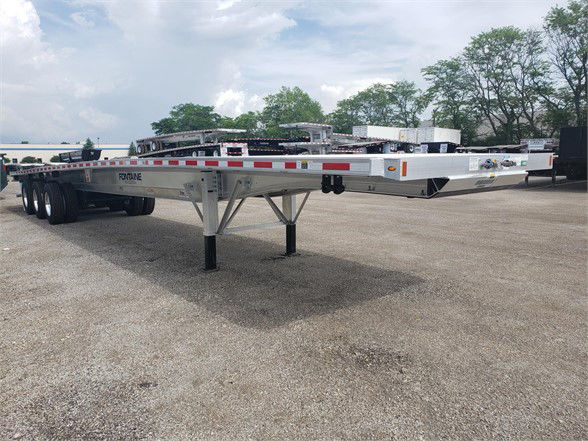 Flatbed trailer showing aluminum frame and tandem axles with Fontaine branding, low to ground, with landing gear and support legs in foreground.