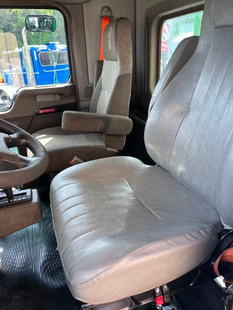 Truck cab interior showing driver seat and passenger seat in a Kenworth T800, grey fabric seats, steering wheel, orange seatbelt shoulder strap visible.