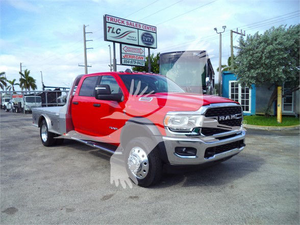 Ram 5500 SLT flatbed truck with red cab and gray front bumper, large side mirrors, chrome grille, dual rear wheels, dealership signage in background
